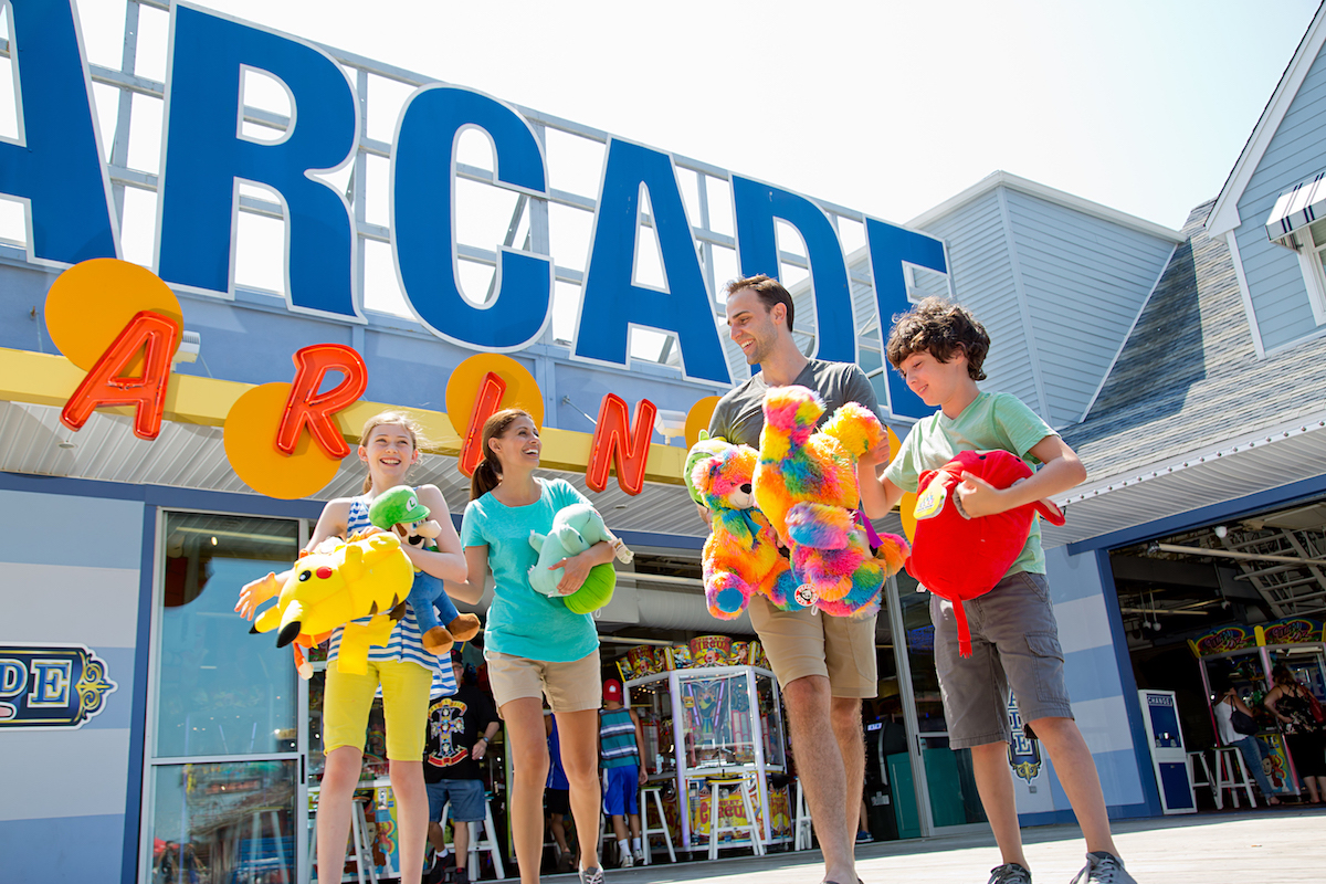 family enjoying the Wildwoods NJ boardwalk in front of arcade holding stuffed animal prizes